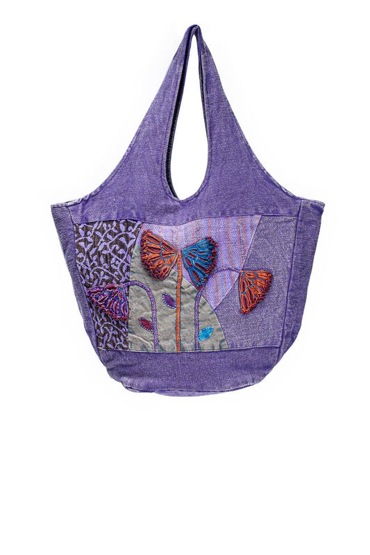 A purple woven fabric tote bag featuring a colorful patchwork front pocket with butterfly and floral embroidery, shown against a plain white background.